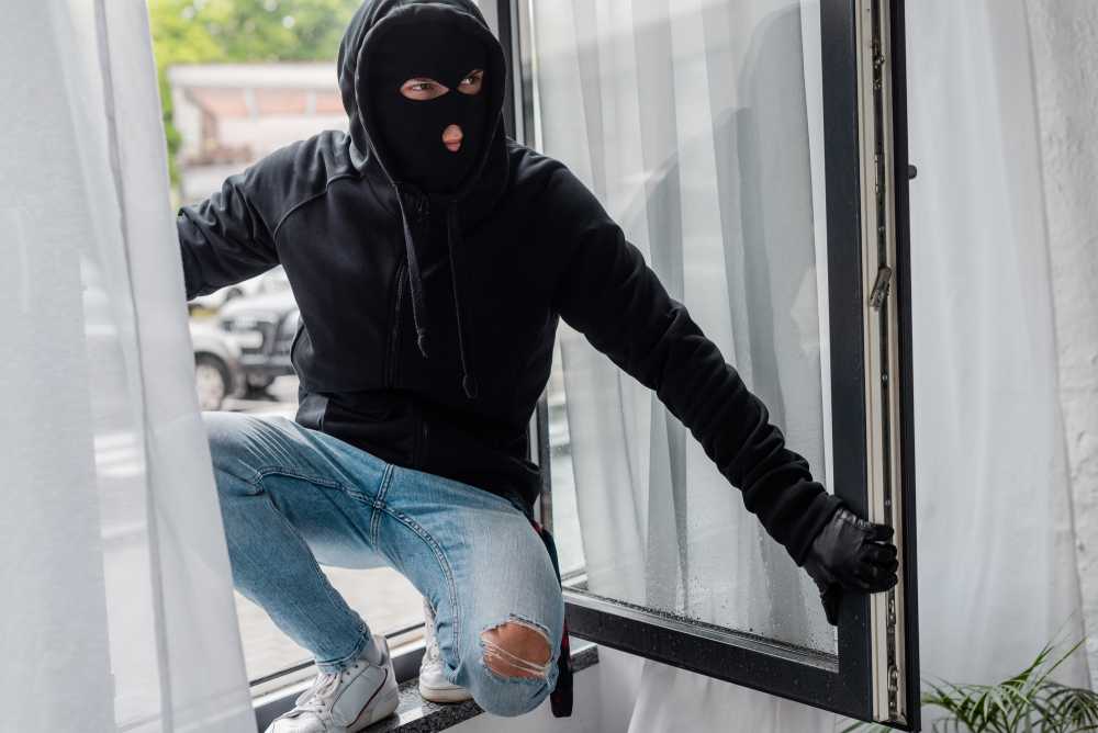 A burglar entering a home due to unlocked windows, one of many common home security mistakes