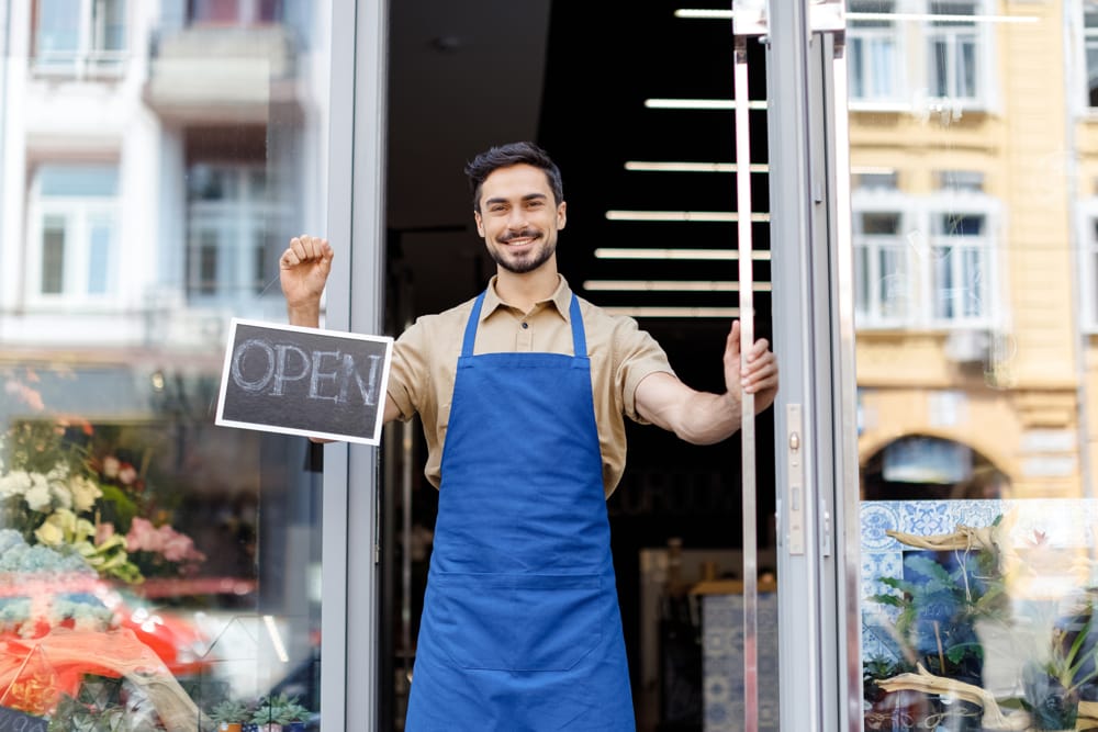 A man standing in front of his small business holding an open sign