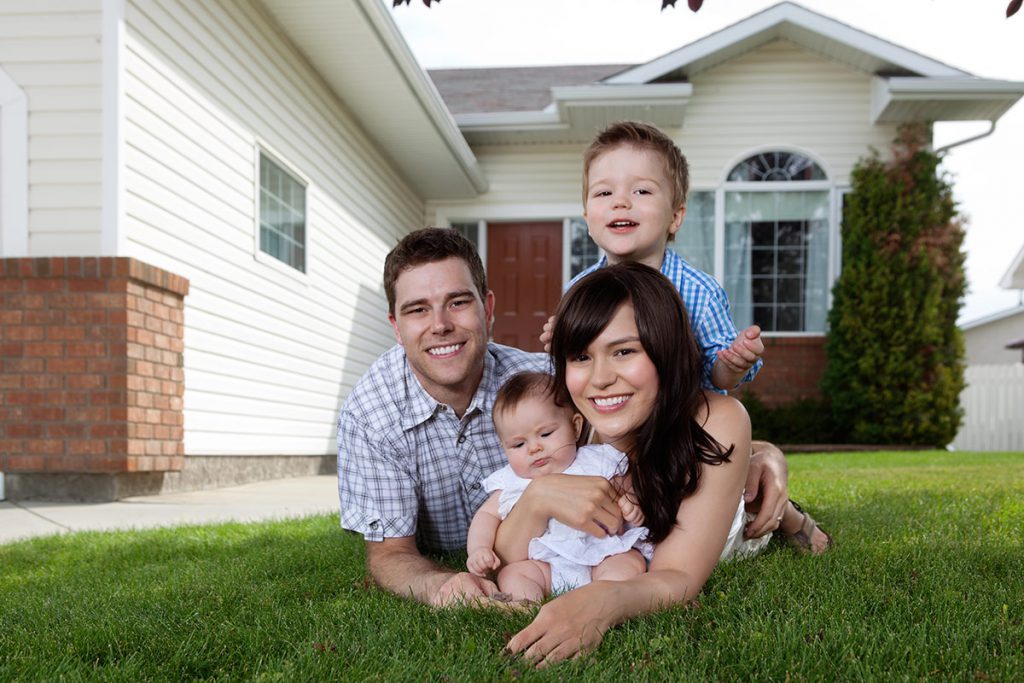 Smiling family of four lying in the grass in front of their home.