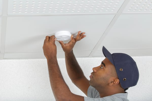 A technician installing a smoke detector and alarm in the ceiling 